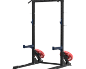 Structure de squat, développé couché ou autres, à deux montants noirs avec barre de traction supérieure, supports J bleus, deux supports de barre, deux axes de rangement de disques, disques bumper rouges de diamètre 51. Vue de ¾